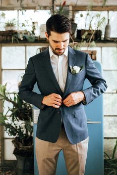 a man in a suit and bow tie is looking down at his pocket while standing next to plants