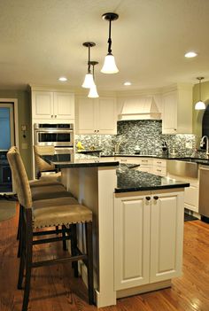 a kitchen with white cabinets, black counter tops and an island in front of the sink