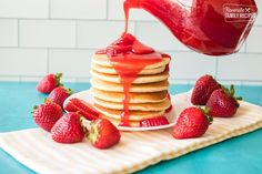 a stack of pancakes covered in syrup and strawberries on a blue table with a white tile background