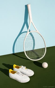 a tennis racket and shoe on the ground next to a ball in front of a blue wall