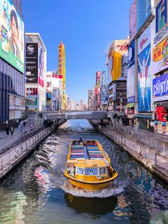 a yellow boat traveling down a river in the middle of a city filled with tall buildings