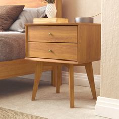 a wooden nightstand sitting on top of a bed next to a night stand with a plant in it