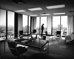 a man standing in an office looking out the window at cityscape and skyscrapers