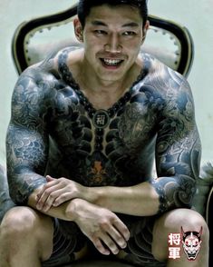 a man with tattoos on his body sitting in a chair and looking at the camera