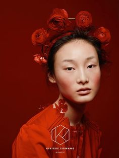 a woman with flowers in her hair and an orange shirt over her head, against a red background