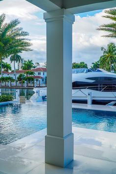 an outdoor swimming pool with palm trees and boats in the water behind it on a cloudy day