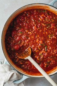 a large pot filled with chili sauce and a wooden spoon