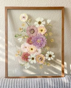 a frame with flowers in it sitting on a couch next to a pillow and wall