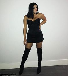 a woman in a black dress and thigh high boots posing for the camera with her hands on her hips