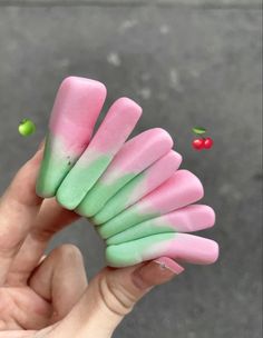 a hand holding up pink and green slimy sticks with cherries in the background