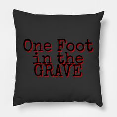 one foot in the grave pillow on a black background with red lettering that reads, one foot in the grave