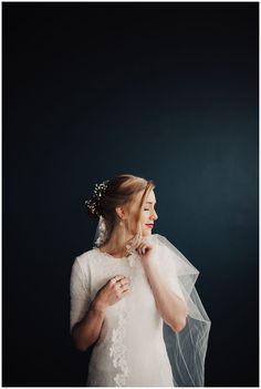 a woman wearing a veil and holding a flower in her hand while standing against a black background