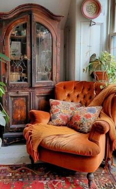 an orange chair sitting in front of a window next to a wooden cabinet and potted plant