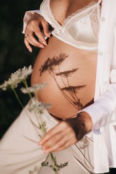 a pregnant woman is holding flowers in her belly while she's wearing a white shirt