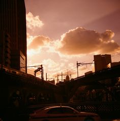 a car is driving down the street in front of a bridge and buildings at sunset