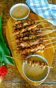 several skewers of food are sitting on a wooden platter with dipping sauce