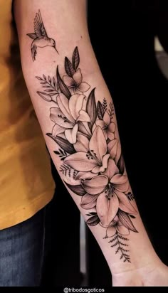 a woman's arm with flowers on it and a bird flying over the top