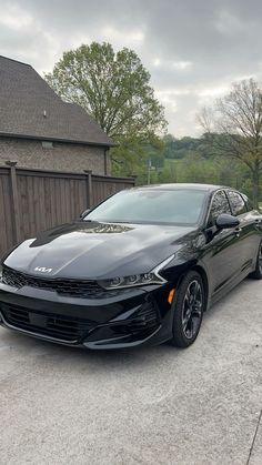 a black sports car parked in front of a house on a driveway next to a wooden fence