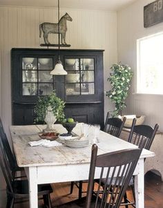 a dining room table with chairs and a china cabinet in the back ground, surrounded by potted plants