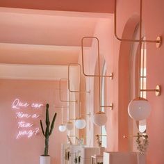 a room with pink walls and white furniture in the center is decorated with hanging lights, vases and cacti