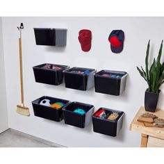 several black bins are hanging on the wall next to a potted plant and broom