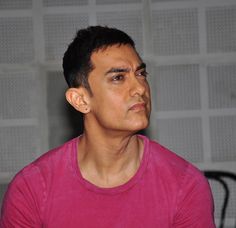 a man in a pink shirt looking off into the distance with an earring on