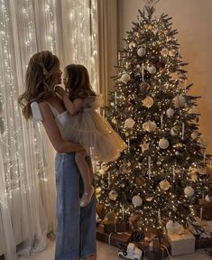 a woman holding a child in front of a christmas tree