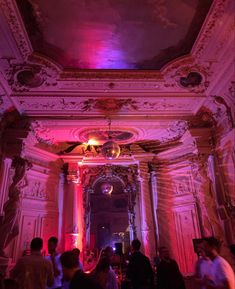 a group of people standing around in a room with pink lighting on the ceiling and walls