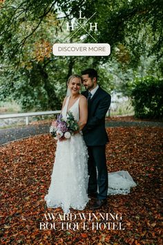 a bride and groom posing for a photo in front of trees with leaves on the ground