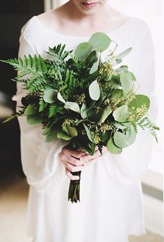 a woman holding a bouquet of greenery in her hands