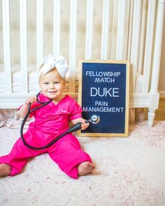 a baby sitting on the floor with a stethoscope in her hand next to a sign that says fellowship match duke pain management