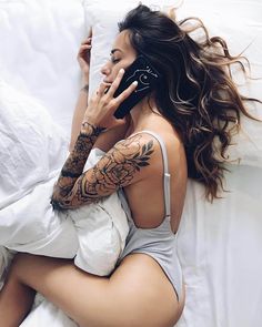 a woman laying in bed talking on a cell phone with tattoos on her arms and shoulder