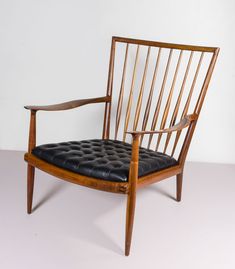 a wooden chair with black leather upholstered seat and arm rests against a white wall