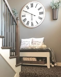 a clock mounted on the wall above a bench with pillows and vases next to it