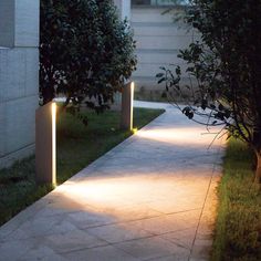 some lights that are on the side of a sidewalk near bushes and trees in front of a building