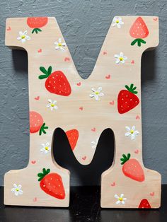 a wooden letter with strawberries and daisies painted on the upper part of it