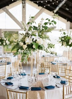 a tall vase filled with white flowers and greenery on top of a round table