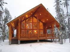 a log cabin in the snow with lights on and stairs leading up to it's second floor