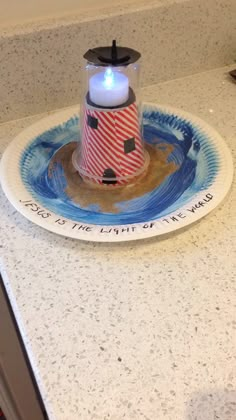 a small lighthouse on a plate with a lit candle in the center and words written below it