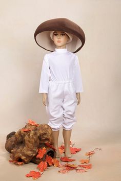 a doll wearing a brown hat and white overalls standing next to a pile of leaves