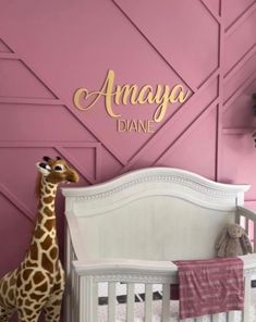 a giraffe standing next to a baby crib in front of a pink wall