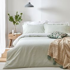 a bed with green and white striped comforter next to a plant in a vase