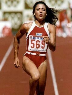 a woman running on a track in a red and white suit with her mouth open