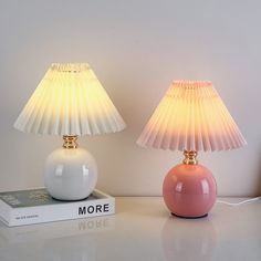 two lamps sitting on top of a white table next to a book and lamp shade