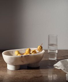 a marble bowl with lemons in it and a glass on the table next to it