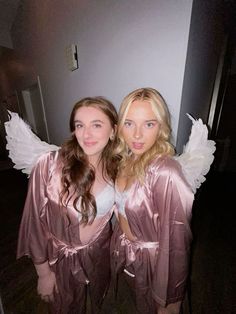 two beautiful young women dressed in pink and white robes posing for the camera with angel wings on their shoulders