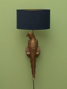 a gold parrot lamp on a green wall with a blue shade over it's head