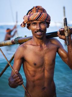 a shirtless man holding two wooden poles in his hands and wearing a turban