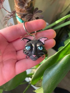 a hand holding a black cat keychain with blue eyes