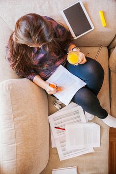 a woman sitting on top of a couch holding a glass of orange juice and reading a book